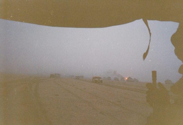 Soldier looking out at military vehicles driving through the desert