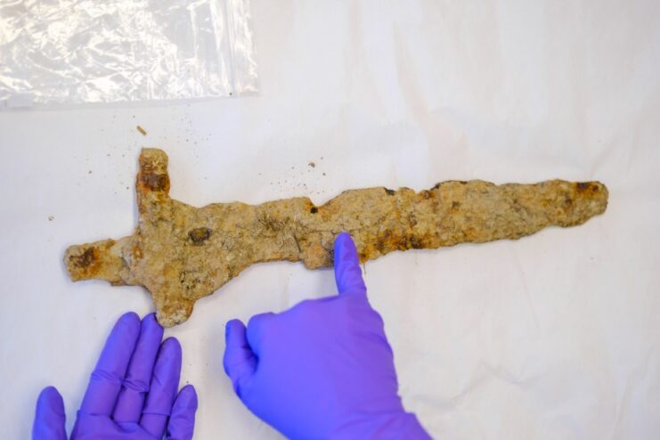 Gloved hands pointing at a Viking Age sword on a white tabletop