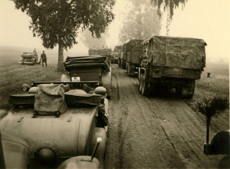 Cars and military vehicles driving down a dirt road