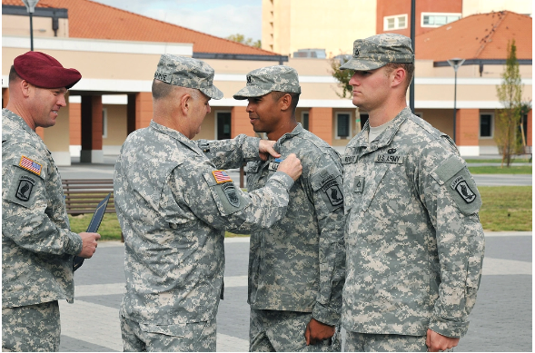 Patrick Donahue pinning the Expert Infantry Badge (EIB) on the uniform of a US Army soldier, while two others stand around them