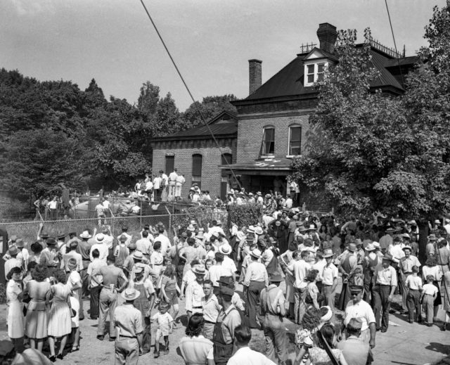 Black and white photo of a large group of people surrounding an old brick building, the Athens courthouse and jail.